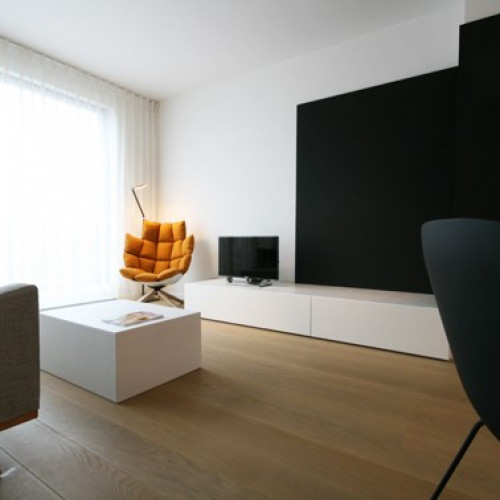 TV-meubel met zwarte achterwand en laag meubel om afstandsbediening, kussens en onderleggers netjes op te bergen.  De bewoners vroegen ons om het interieur een extraatje te geven. Wij stelden deze oranje zetel voor als uniek accent, een idee dat zij meteen zagen zitten, letterlijk en figuurlijk! Kast-ID Antwerpen